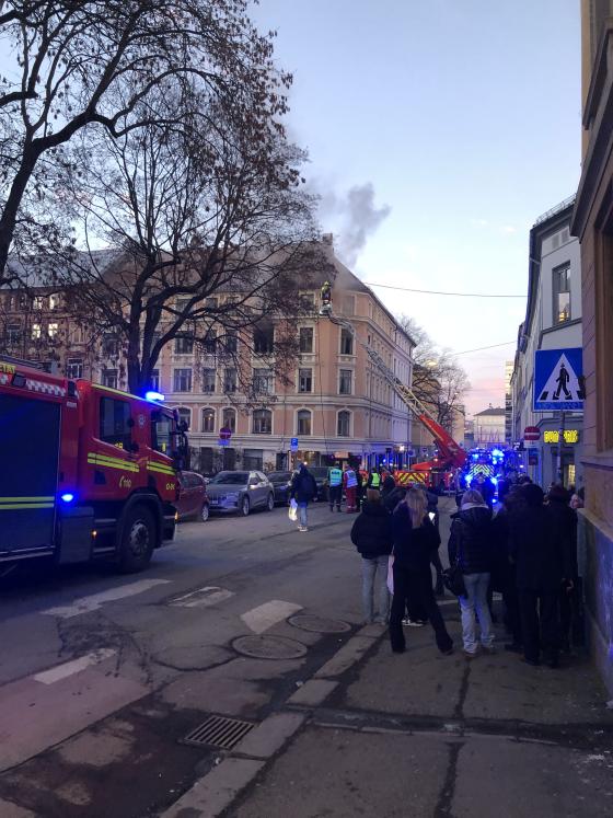 Bygningen det brant i i Møllergata, tatt fra fortauet over veien litt bortenfor bygget. Mørkegrå røyk stiger ut fra et vindu i 4. etasje, der vinduene er borte og det ser helt svart ut inni. Bortsett fra det ser bygårdens fasade ganske dagligdags ut.