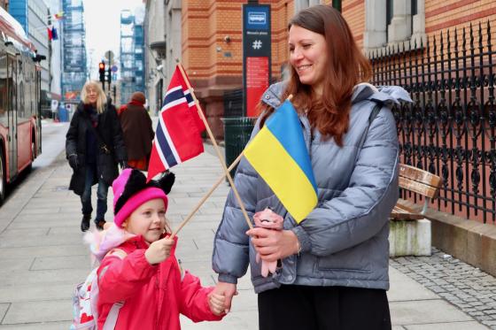 mor og datter på et fortau som holder det norske og det ukrainske flagget i kryss og smiler