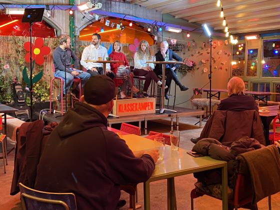 Fem mennesker sitter på en scene og debatterer. 