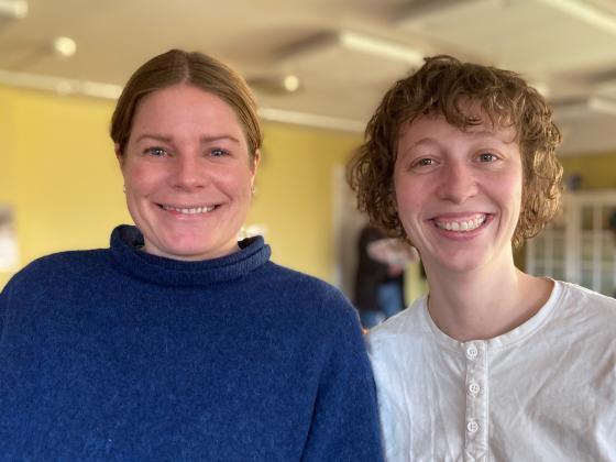 Portrettbilde av Ingrid Kristiane Fardal og Susanne Rude Lone, som smiler inne i Sogn frivilligsentral. Bak dem er grønne vegger og hjemlige gjenstander. 