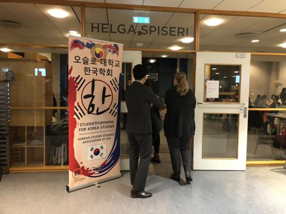 Tre personer går inn døren til en kafeteria. Ved siden av er banneret til Korean Studies Student Association