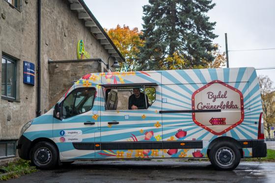 Foodtruck står plassert utenfor bygg med ansatt som ser ut av luken i bilen.