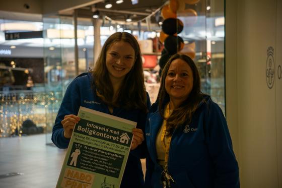 Two women in blue sweaters holding a poster.