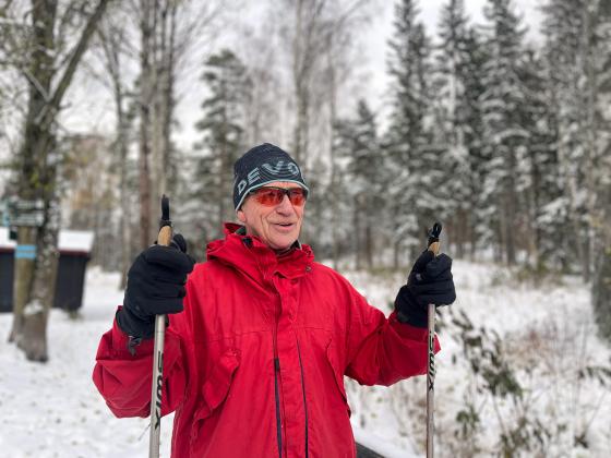 Eldre mann som er ferdig med skituren. Han har på en rød anorakk og en skistav i hver hånd. 