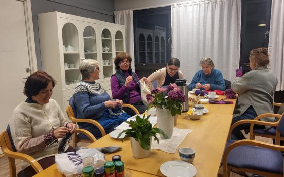 Seks damer på Sagene Frivilligsentral sin strikkekafé, som sitter rundt et bord og drikker kaffe og strikker.