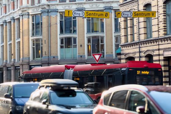 Bilde av trafikken. I forvei er det biler ute av fokus. Over en rød buss ser man veitrafikkskilt med teksten "Ring 1 Sentrum Øst" som peker frem og "Ring 1 Sentrum Vest" som peker til høyre