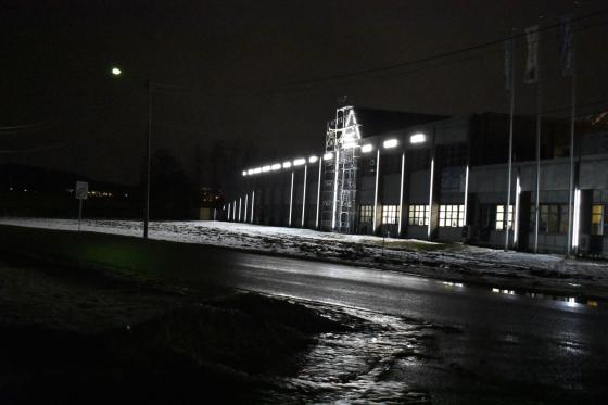 En bygning i en næringspark med logoer lyser opp veien og jordet foran seg. Lysene er hvite og sterke. 