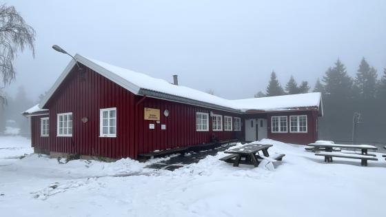 En rød hytte med lys snø på tak og omkring