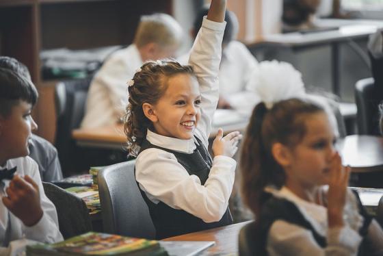 smilende skolepike rekker opp hånden i klasserommet