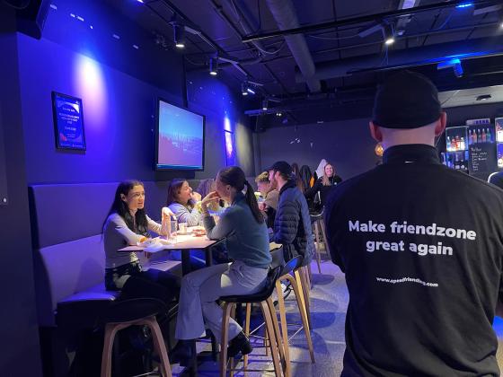 Victor Sanden (35) står foran bord med speed friending deltakere. Han har slagordet "Make friendzone great again" bak på genseren. 