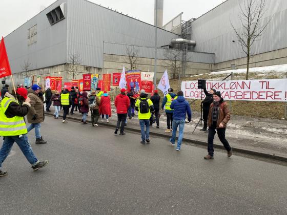 Mennesker går over veien, skilt og bannere i bakgrunnen