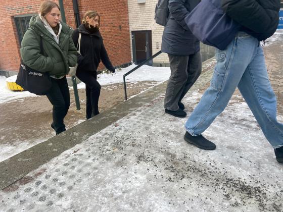 Studenter som går over en is- og grusbelagt vei.