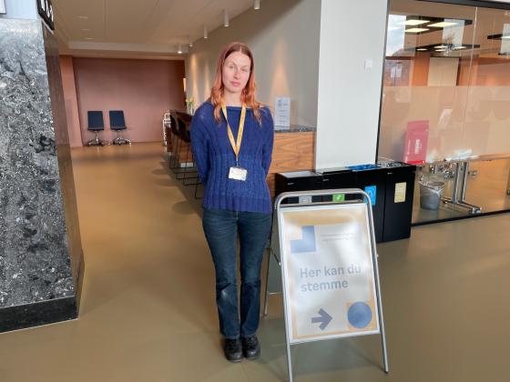 Valgmedarbeider Sunniva Harstein står bak en plakat med teksten "Her kan du stemme".