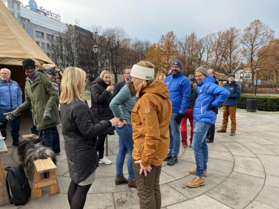 Politikere og representanter fra Norsk Friluftsliv står samlet utenfor Stortinget ved en lavo og et bord med kaffe og gløgg. 