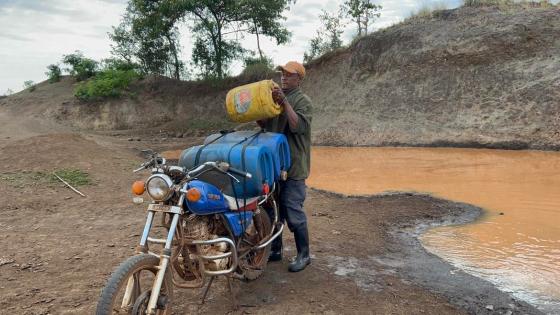 Bilde av en mann i Afrika som samler skittent vann i plastdunker fra en bekk