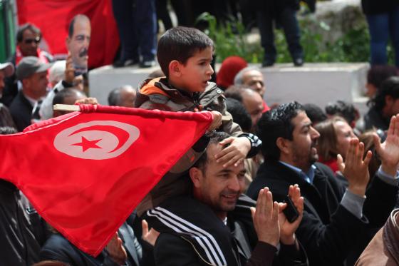 Barn som sitter på farens skuldre med et tunisisk flagg