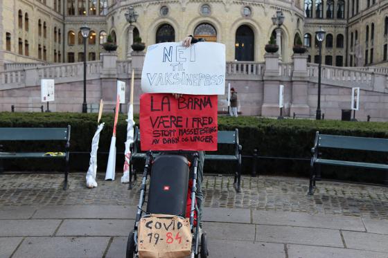 En demonstrant fra Røde Luer skjuler seg bak plakater mot vaksinepass