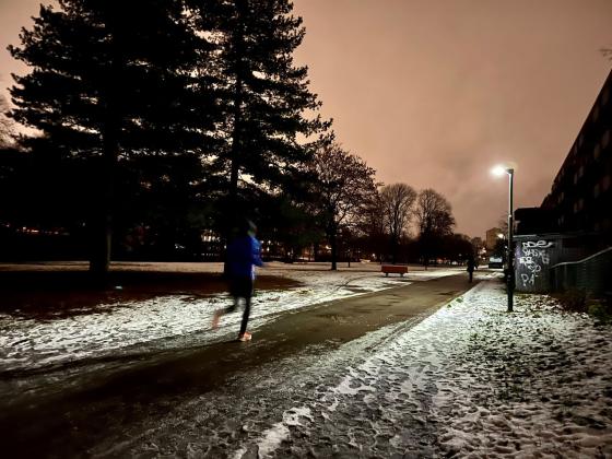 Det er mørkt ute og mann jogger forbi på en vei med snø