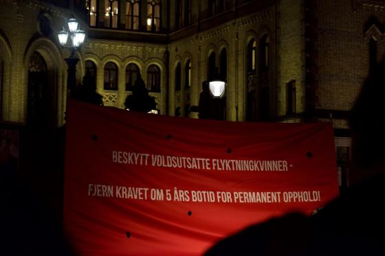 Rød banner på plassen foran Stortinget der det står beskytt voldsutsatte flyktningkvinner fjern kravet om fem års botid for permanent opphold