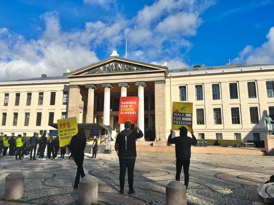 Tre personer står med ryggen til og viser plakater