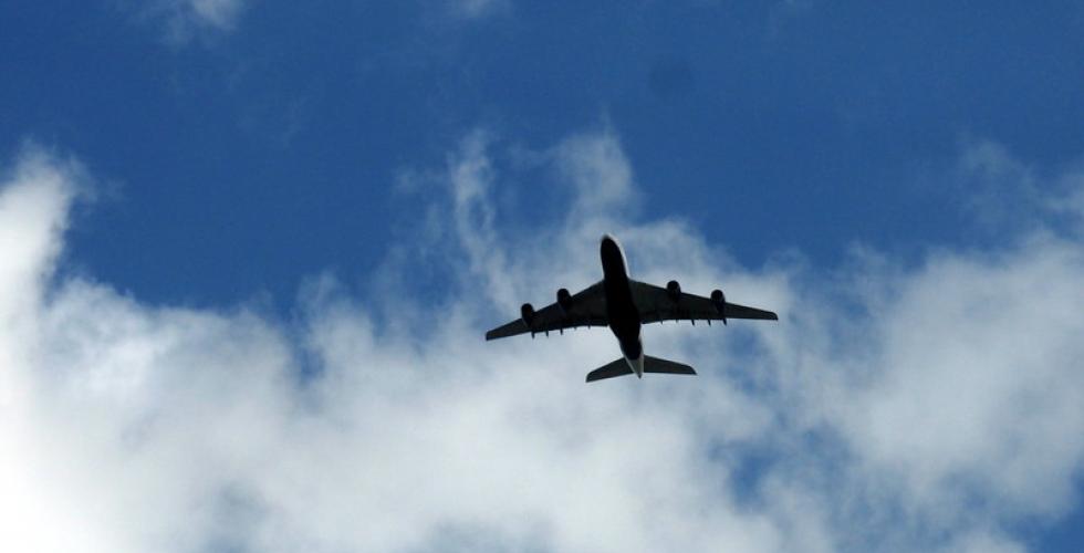 Bilde av et fly tatt underfra, blå himmel og skyer i bakgrunnen.