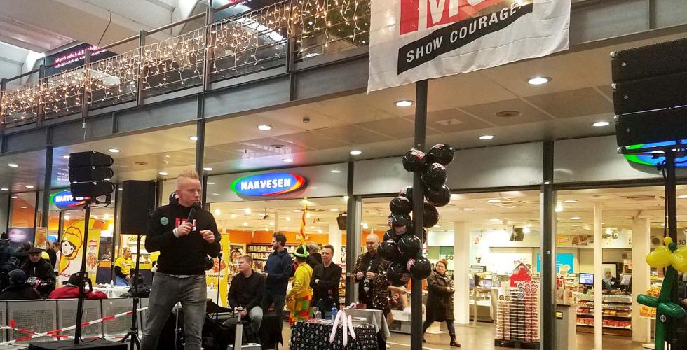 Konferansier for "Mot til å glede-dagen" står på scenen foran Narvesen på Oslo S.