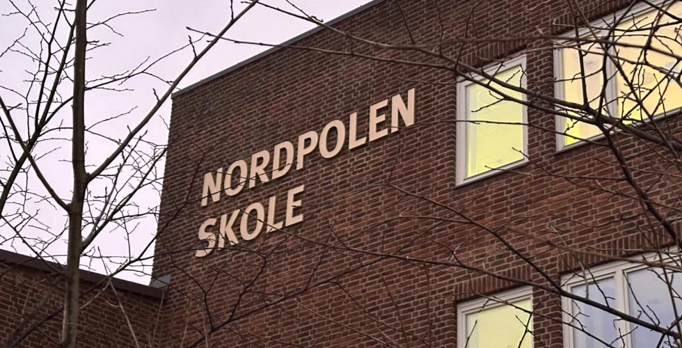 Bide av Nordpolen skole med litt tre uten blader på siden. Vi ser godt nordpolen skole skiltet