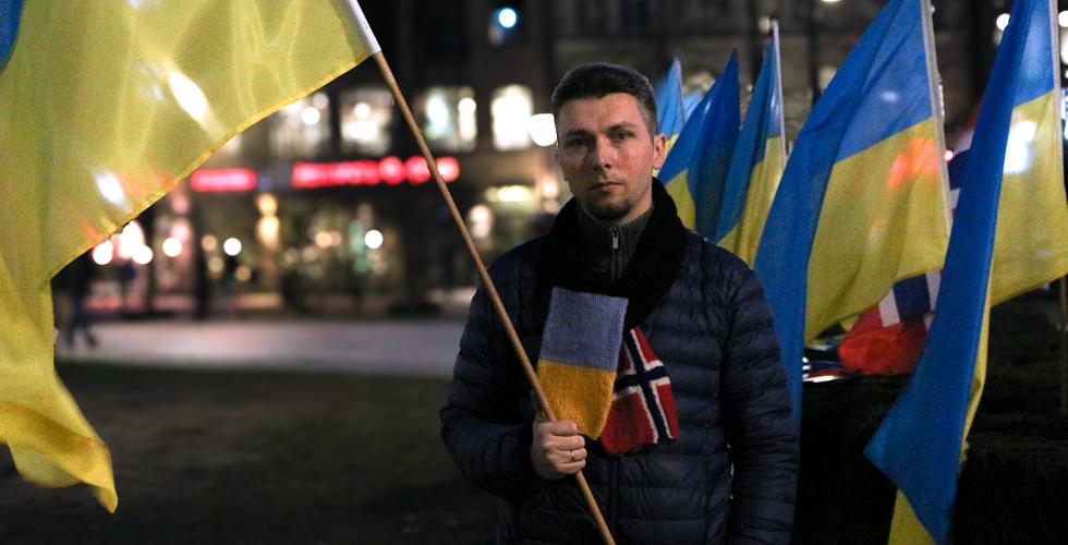 Rostyslav Yevdiukhin står på Eidsvoll plass mens han holder en flaggstang med et Ukrainsk flagg