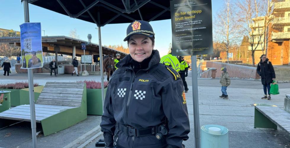 Politibetjent står foran en stand på Mortensrudtorget og smiler