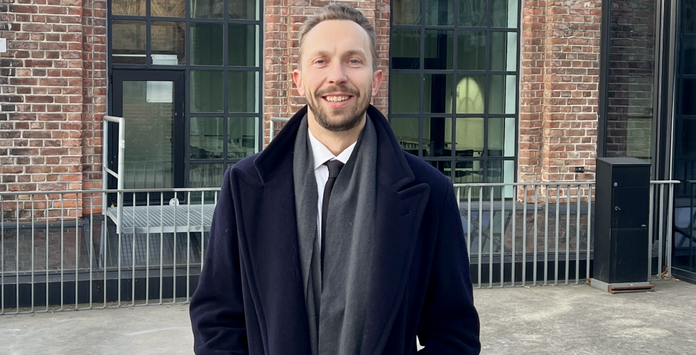 Mann i frakk smiler foran Kunsthøgskolen i Oslo