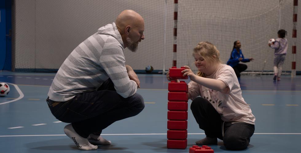 Far og datter som leker med store legoklosser sammen i en idretshall. 