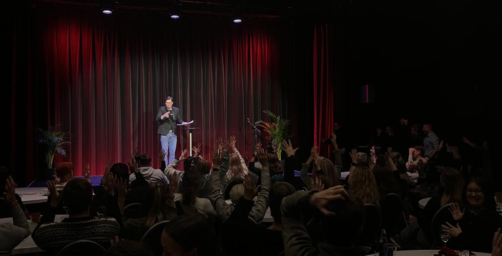 En mann står på scenen og snakker tegnspråk, men publikum et fullsatt applauderer