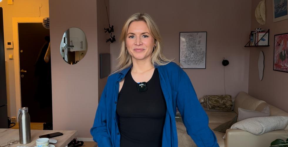 Kornelia Minsaas står i stuen sin ikledd en blå skjorte