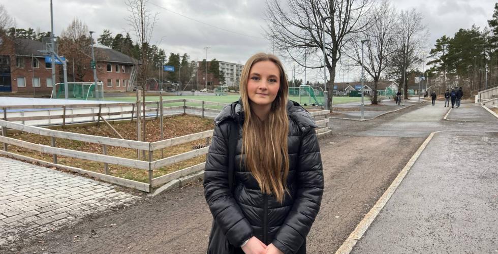 Jente som står i skolegård med hendene foldet