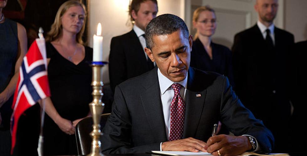 Obama sitter og skriver under en avtale med et norsk flagg i bakgrunnen