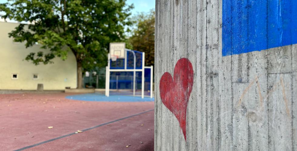 Et hjerte på en vegg, med en basketball bane i bakgrunnen i en skolegård