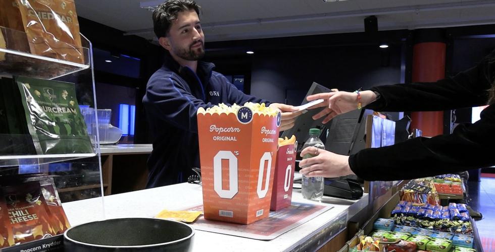 Mann selger popcorn til kunde. På kino. 
