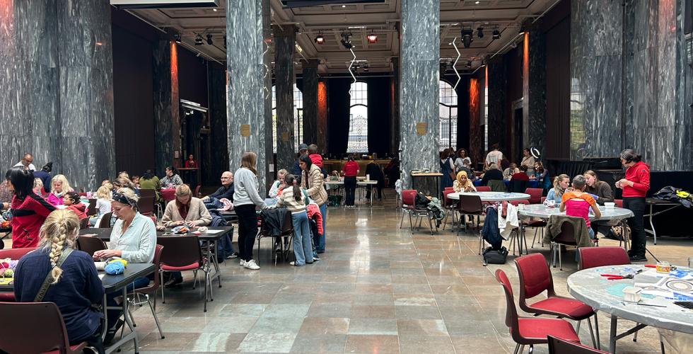 Deltakerne på Håndverksdagen på Sentralen er samlet rundt bord i Marmorsalen hvor de holder på med ulike typer håndverk. 