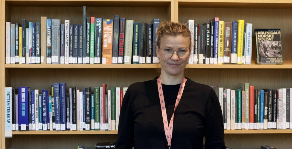 Frid Hamsun står foran en bokhylle. Hun er seksjonsleder på Deichman Lambertseter