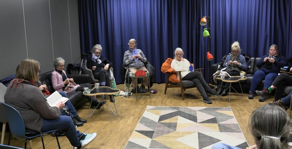 Personer sitter i ring og strikker.