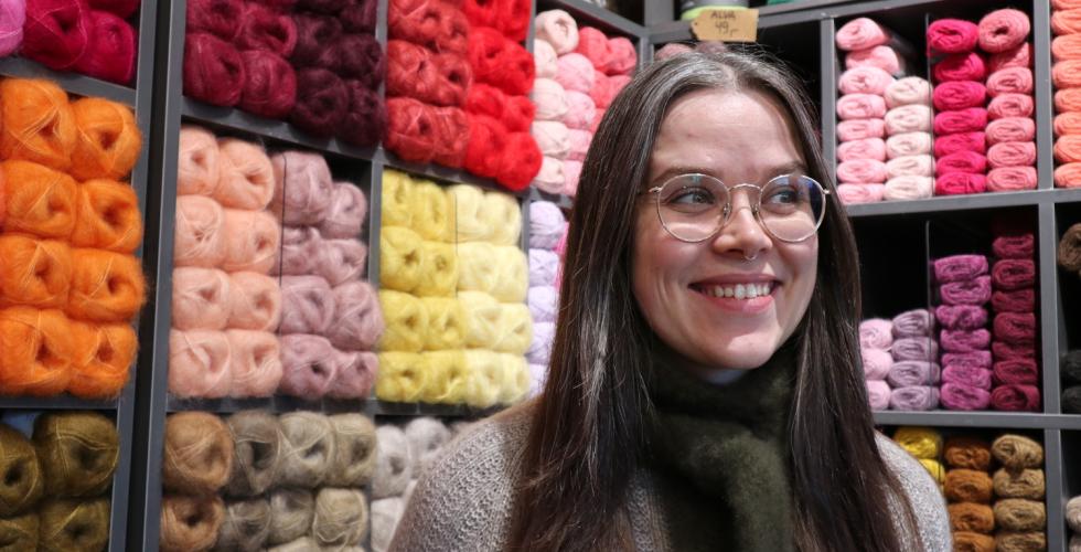 Dame som står foran en vegg av garn og smiler