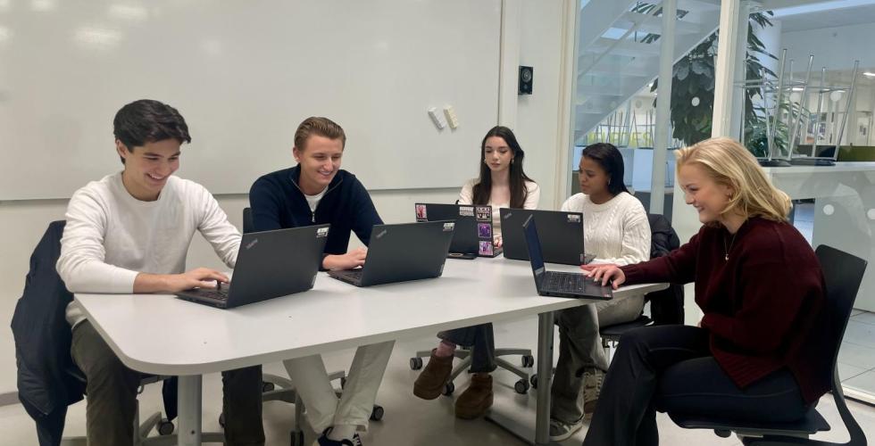Fem elever sitter på et grupperom og arbeider.