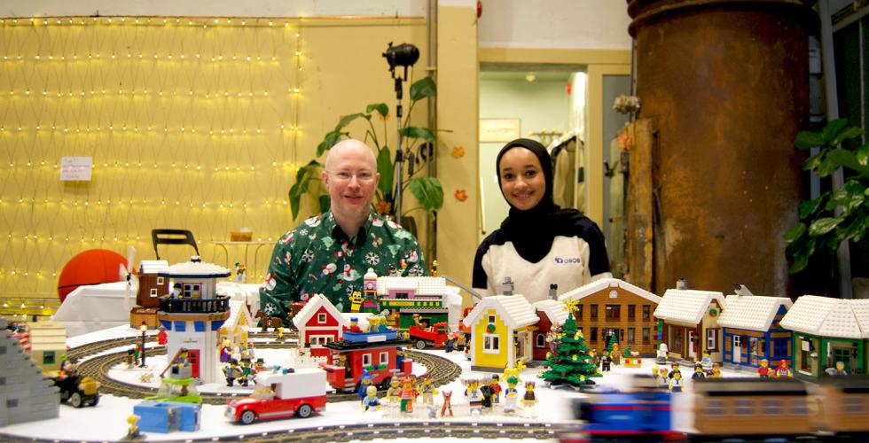 Jaleela og Roy sitter foran utstilling på lego-marked. 