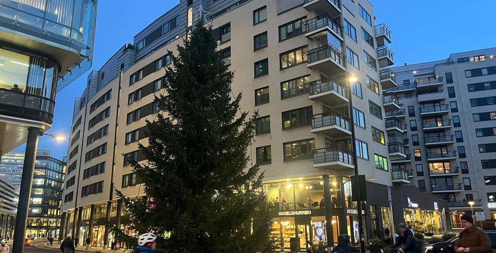 Et juletre foran starten av Karenlyst Allé rett utenfor togstasjonen på Skøyen. Folk går forbi. Det er litt mørkt. 