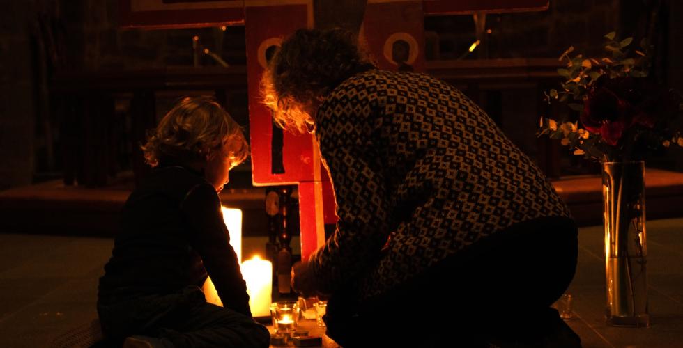 Et barn tenner lys med bestemor foran korset i Gamle Aker kirke.