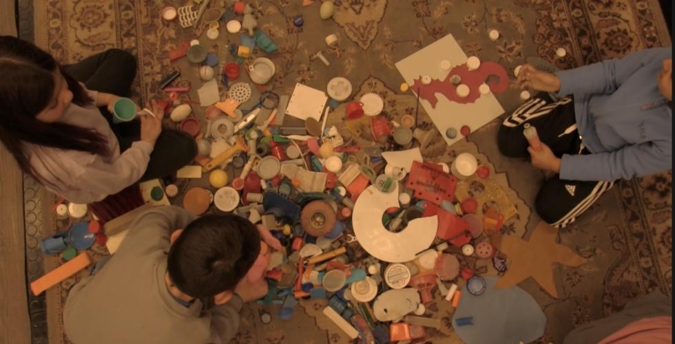 Tre barn sitter rundt en haug med fargerik og ren søppel