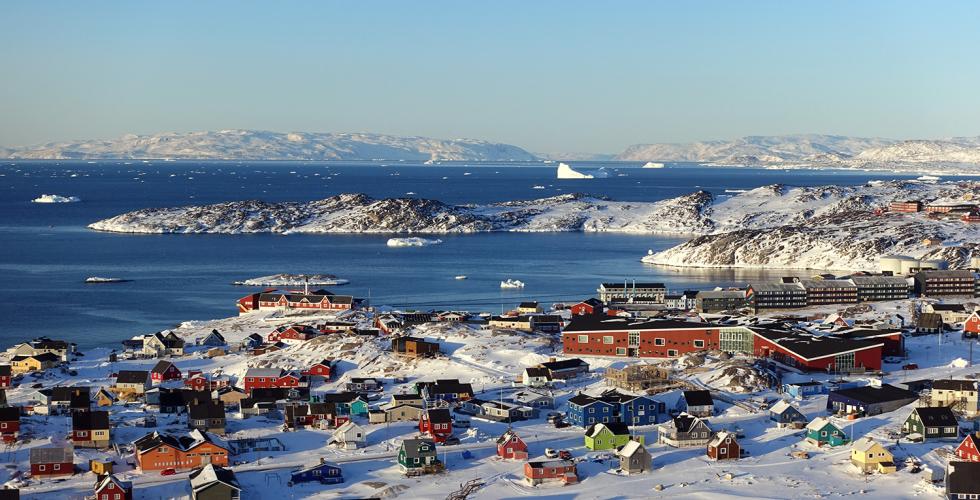 Fargerike hus st&aring;r i sn&oslash;dekket landskap. Det er mulig &aring; se hav og fjell