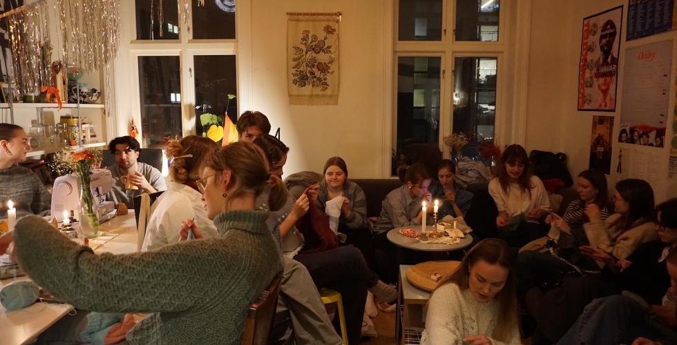 Full stue med mennesker som b&aring;de syr, strikker og snakker. 