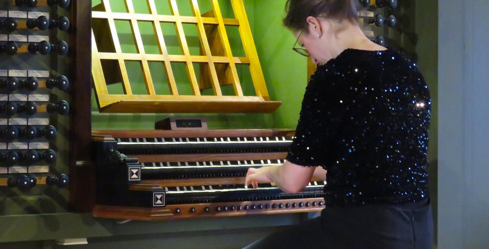 En svartkledd kvinne sitter og spiller orgel med ryggen til.