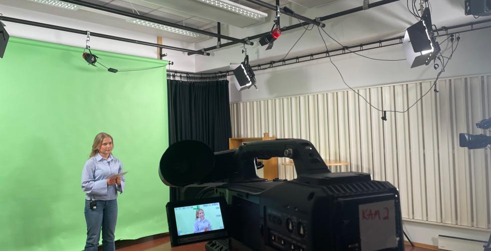 Kvinne foran greenscreen med kamera siktet p&aring;